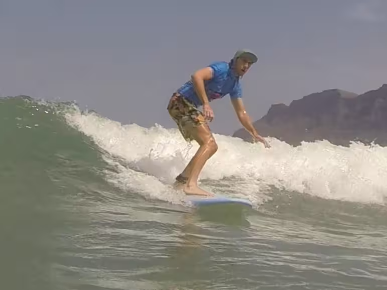 A surfer  in a surflesson for intermediate and advanced surfers is riding a greenwave backhanded. Positioned in the pocket to harvest momentum for the next turn.