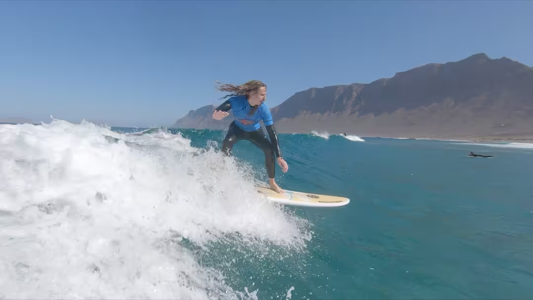 A young woman riding a head-high wave, right after taking off, in a surf lesson for intermediate and advanced surfers.