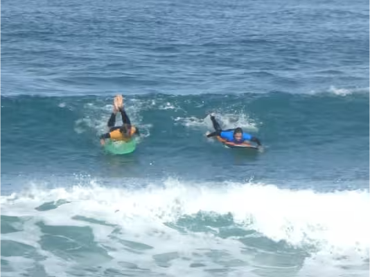 A surfer working paddeling for a green wave, guided by his coach, right before the take off.