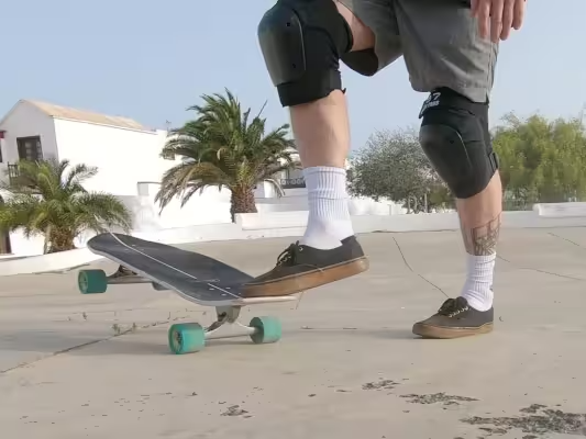 Close-up showing a surfskate board, a skater’s shoes and legs as he rotates the board into the starting position with one foot.